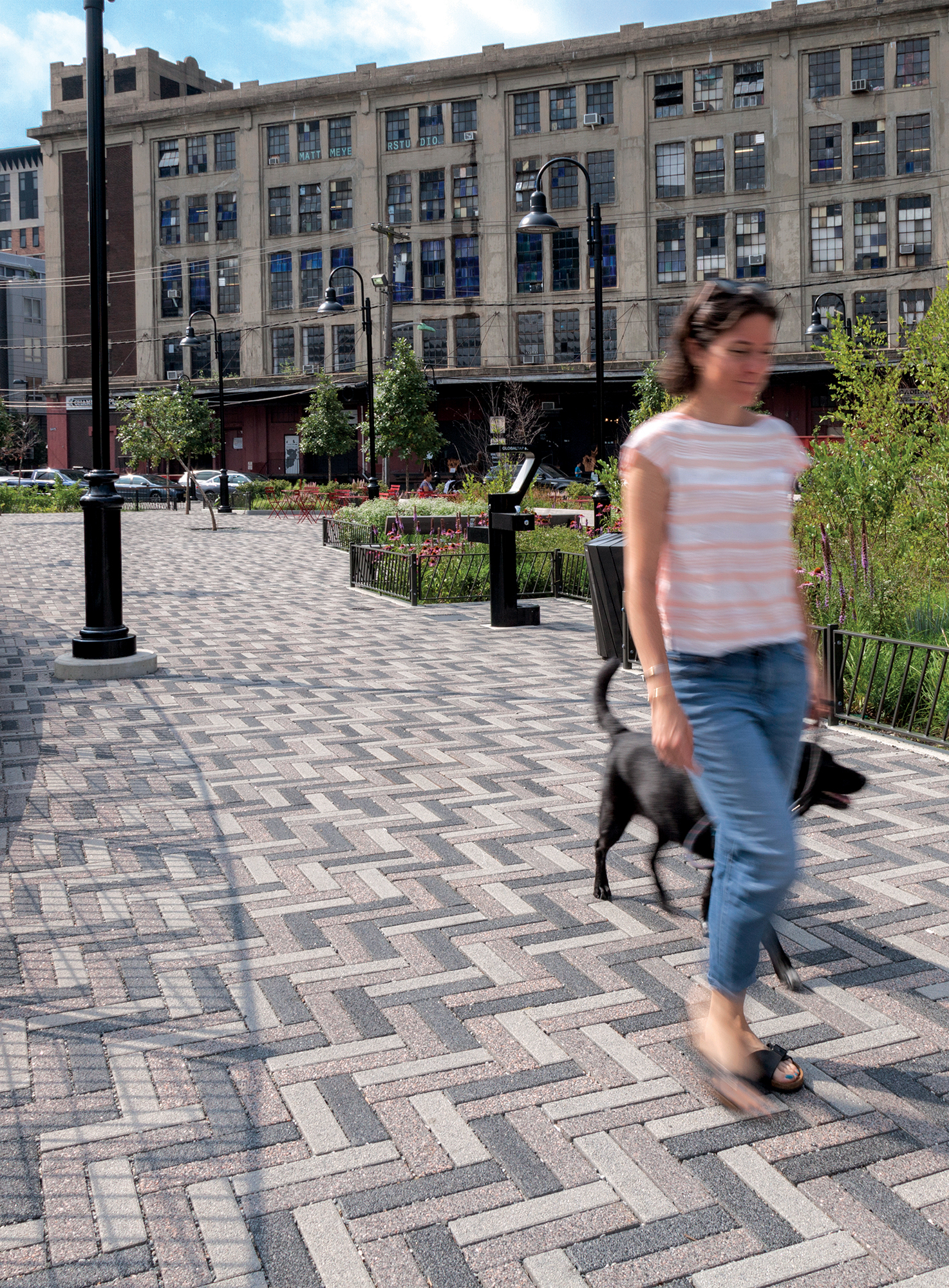 A person walks a dog along a route with Eco-Promenade pavers in three distinct hues arranged in a zigzag pattern to add visual interest.