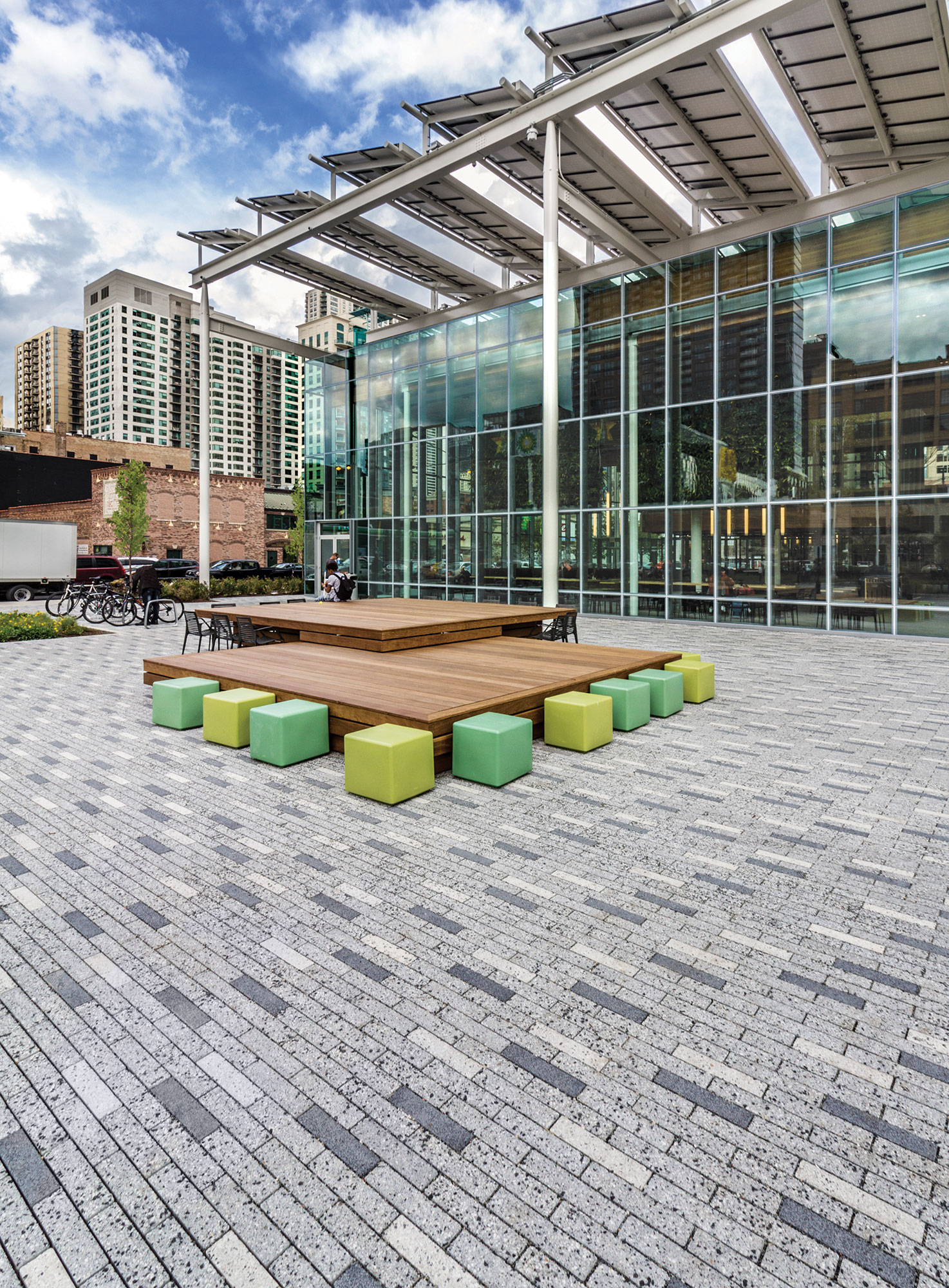Eco-Promenade permeable pavers in different tones from white to dark grey with a speckled finish hold colorful seating blocks and tables.