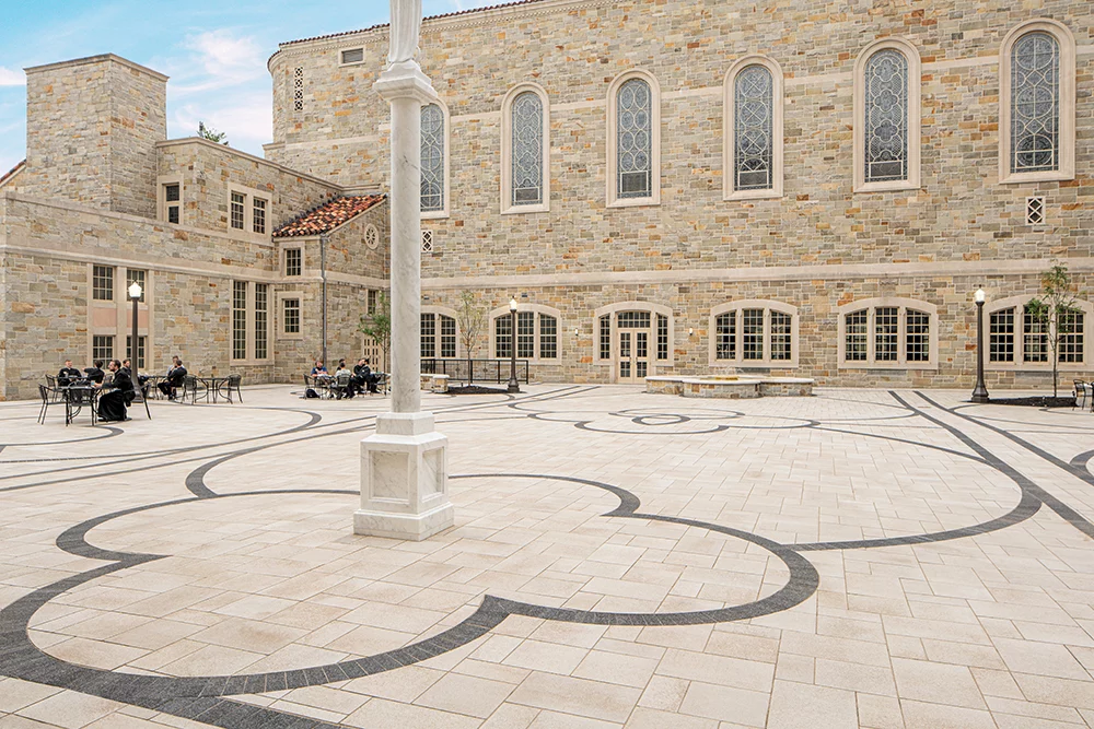 Abstract tan and charcoal paver pattern in a courtyard of a tan building.