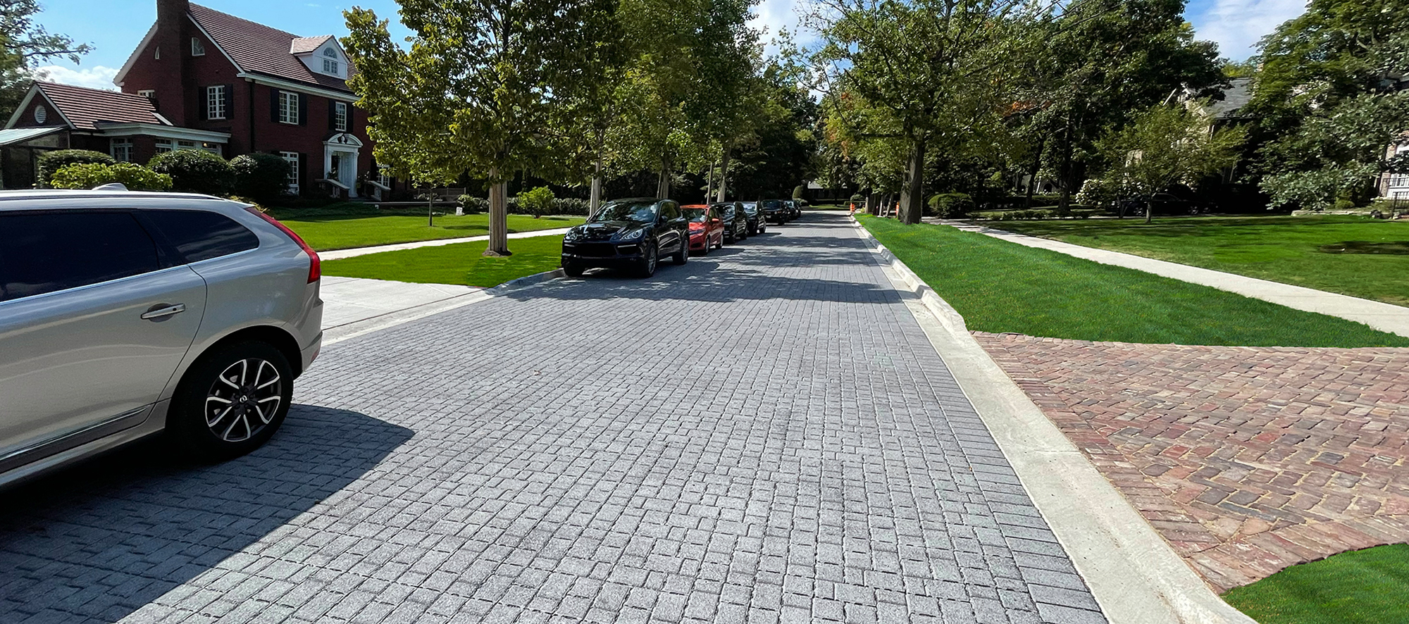 down the middle of a quiet neighbourhood street is a grey roadway paved in unilock eco-optiloc with lush grass on either side.